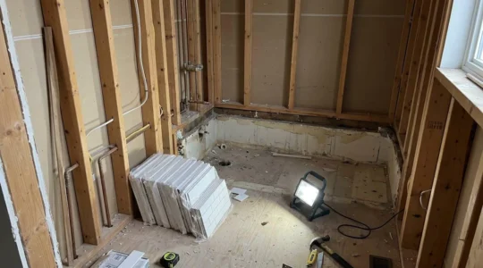Salle de bain résidentielle en cours de rénovation avec murs dénudés exposant la charpente de bois et le sous-plancher